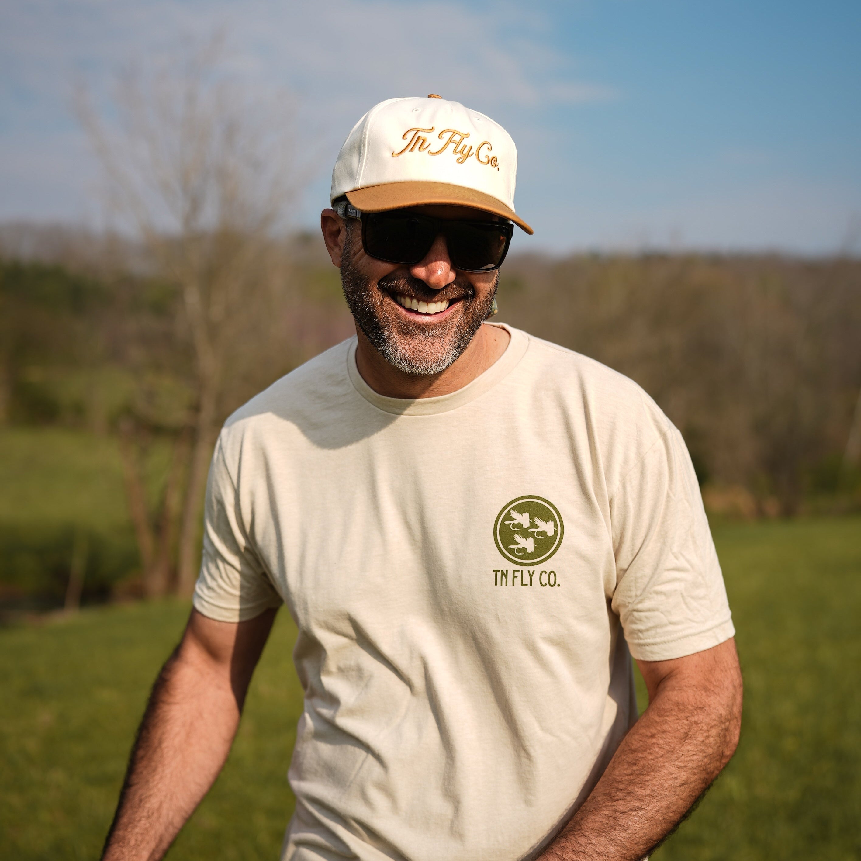 Man wearing a white cap and t-shirt with a logo, standing outdoors.
